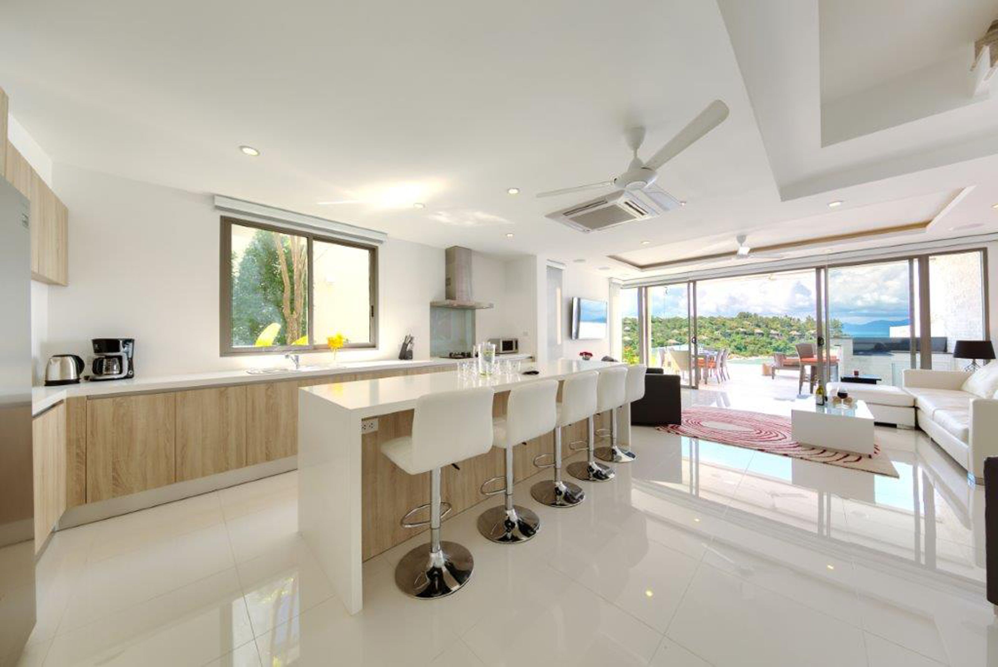Una cocina moderna con una isla central, taburetes de bar y un ventanal amplio.