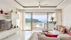 Una sala de estar moderna con televisor, sofá y comedor, que cuenta con un amplio ventanal corredero a un balcón con vistas panorámicas.