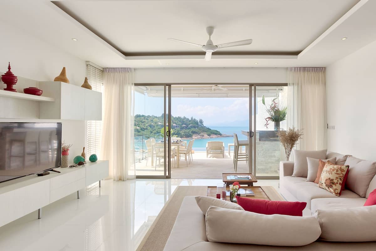 Una sala de estar moderna con televisor, sofá y comedor, que cuenta con un amplio ventanal corredero a un balcón con vistas panorámicas.
