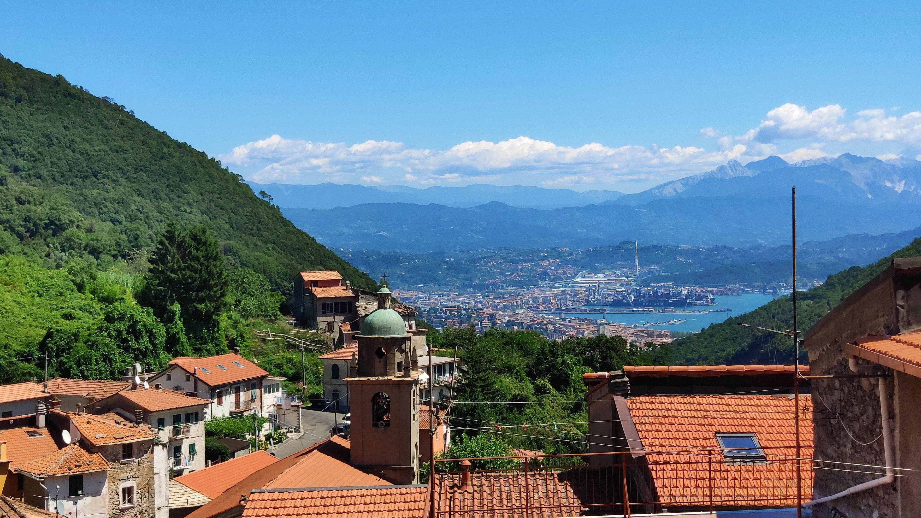 Eine Stadt mit terrakottafarbenen Dächern, einer Kirche mit einer grünen Kuppel und einem Blick auf eine Stadt und Berge in der Ferne.