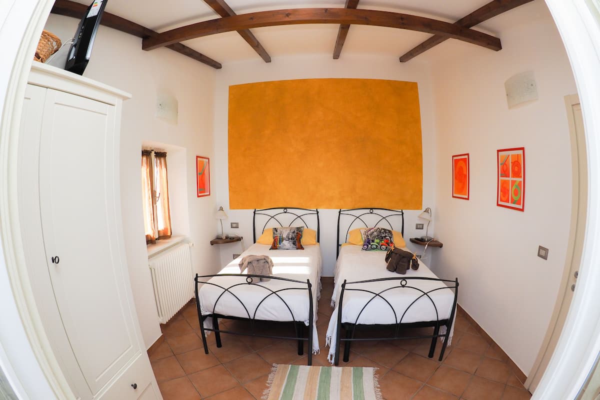 A room with two beds, a white wardrobe, a radiator, and a large orange wall.
