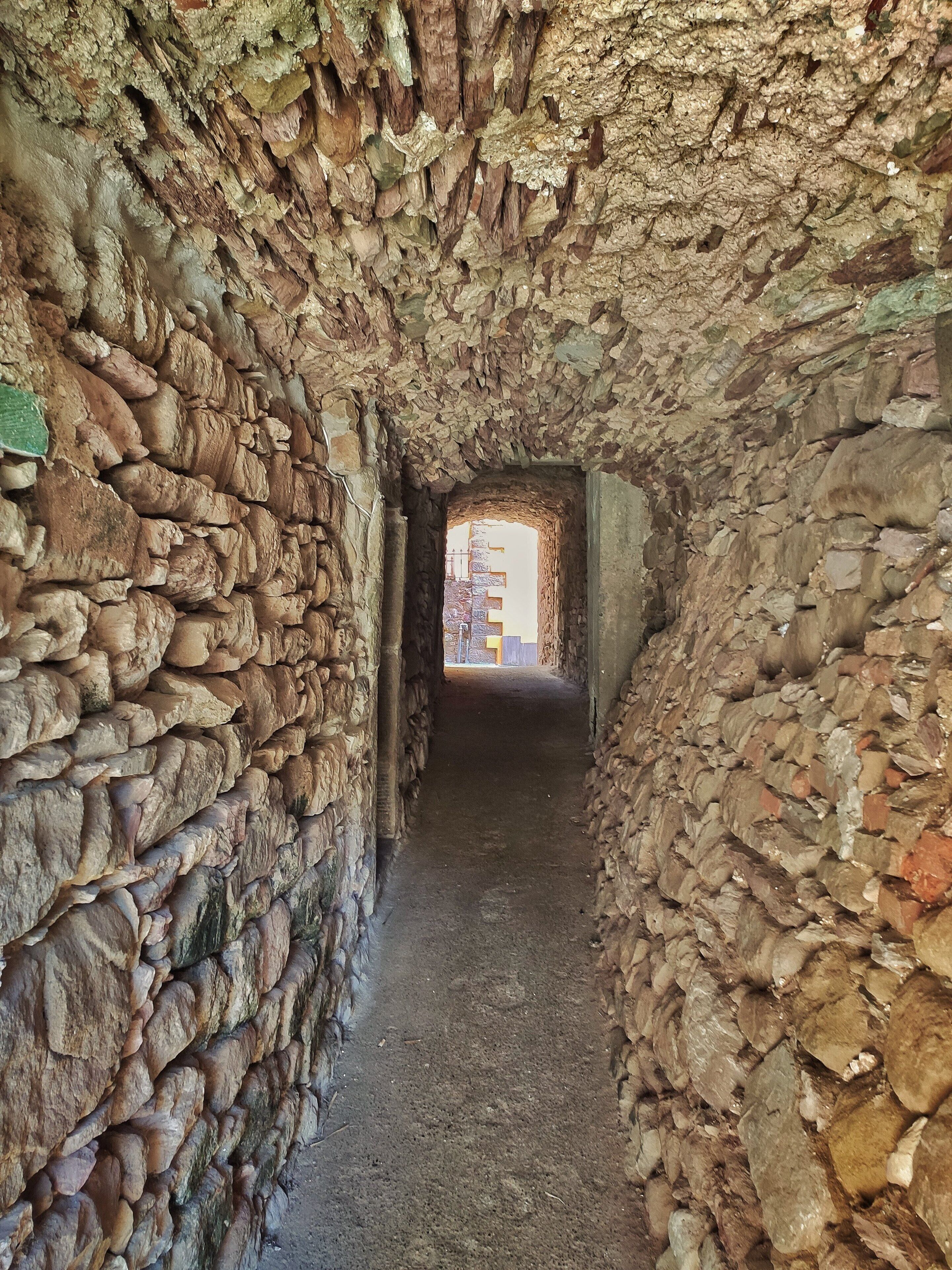 A stone corridor with rough, uneven walls and a narrow pathway leading to a doorway.