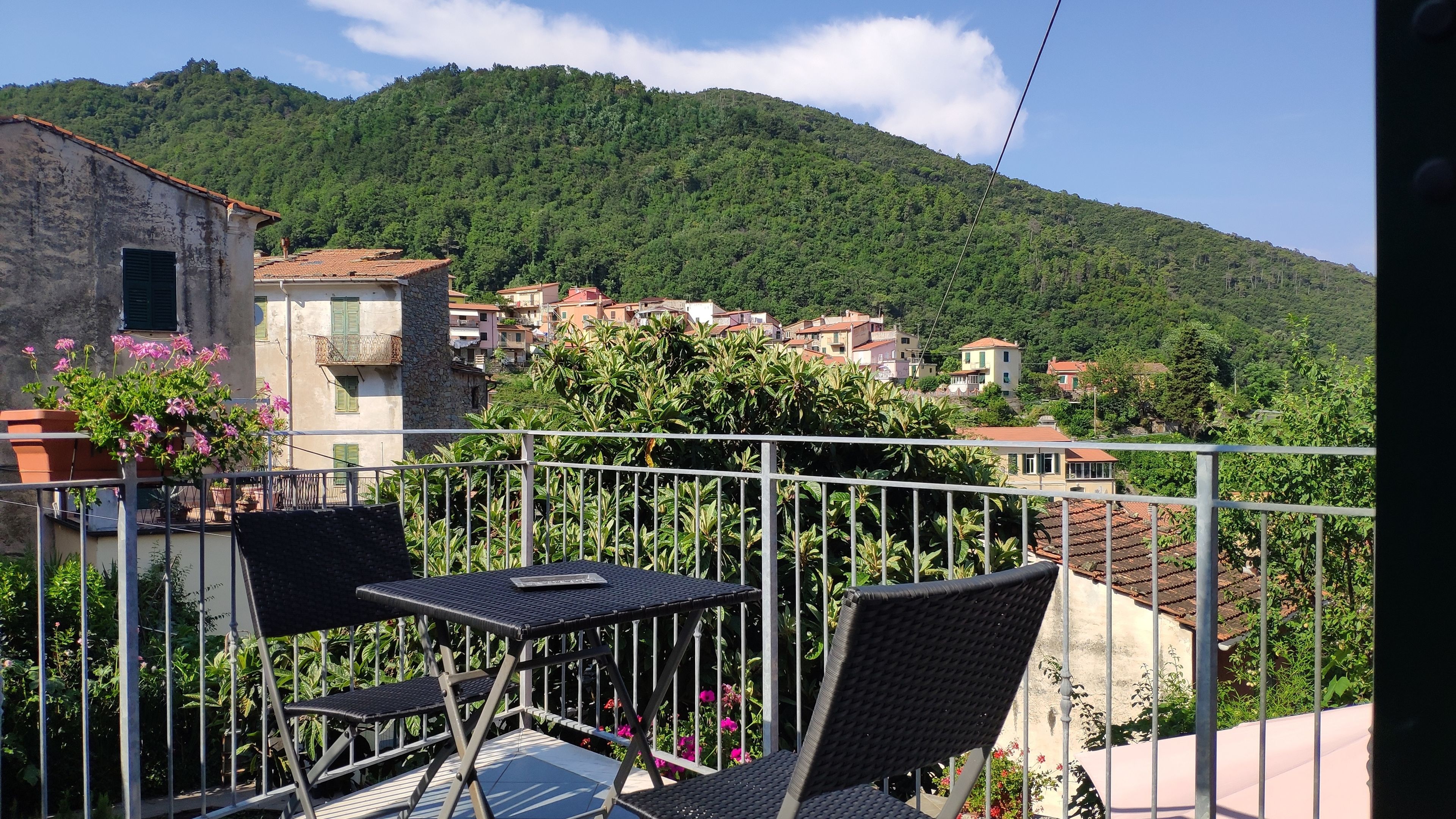 A balcony with outdoor furniture, a view of a hillside with buildings, and a clear sky.