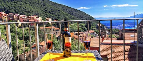Un balcón con una mesa lista para dos personas, con una botella y copas de vino, con vistas a un pueblo en la ladera.
