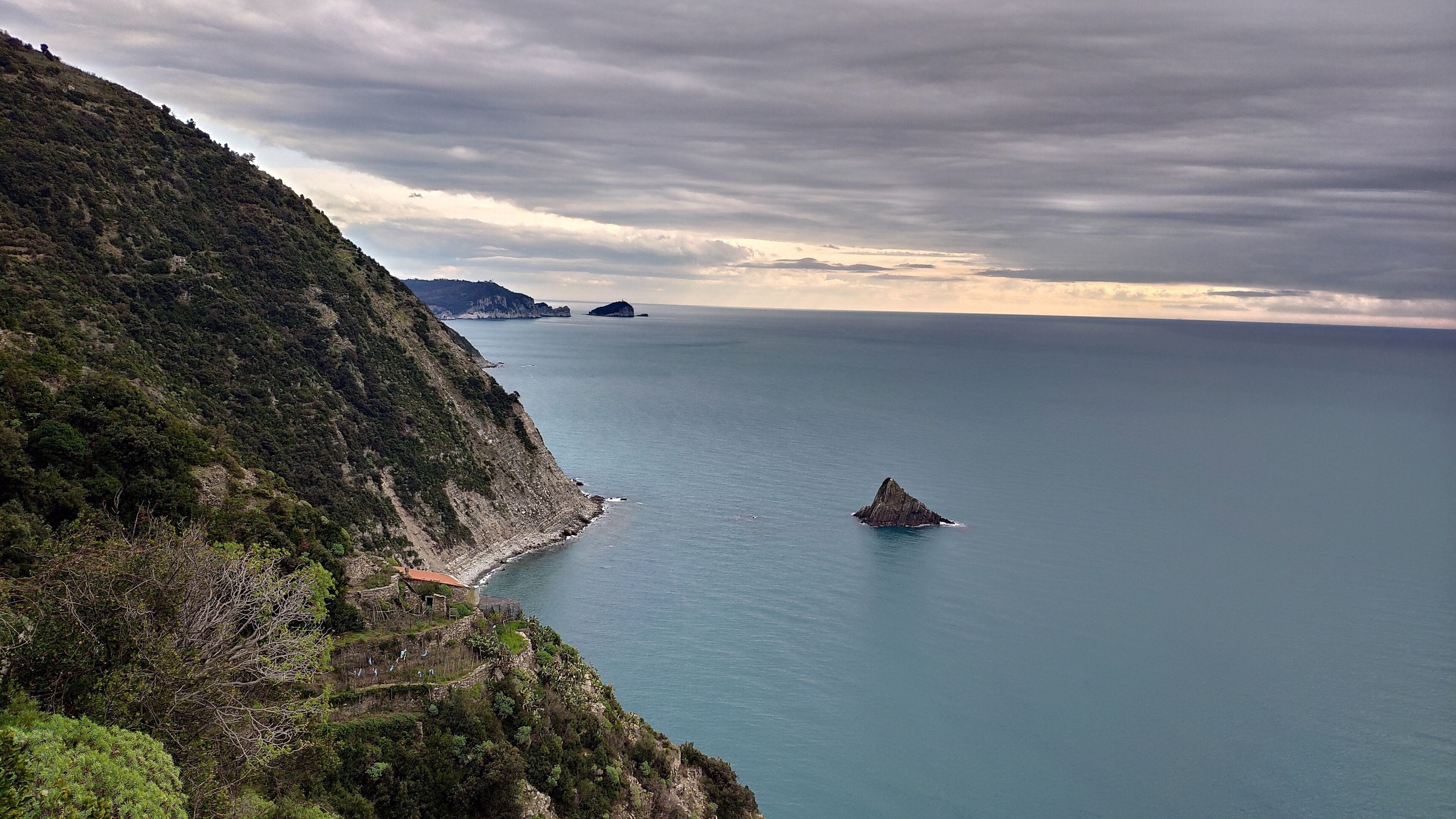 A coastal landscape with a rocky outcrop in the sea, a cliff with sparse vegetation, and a distant view of a small island.