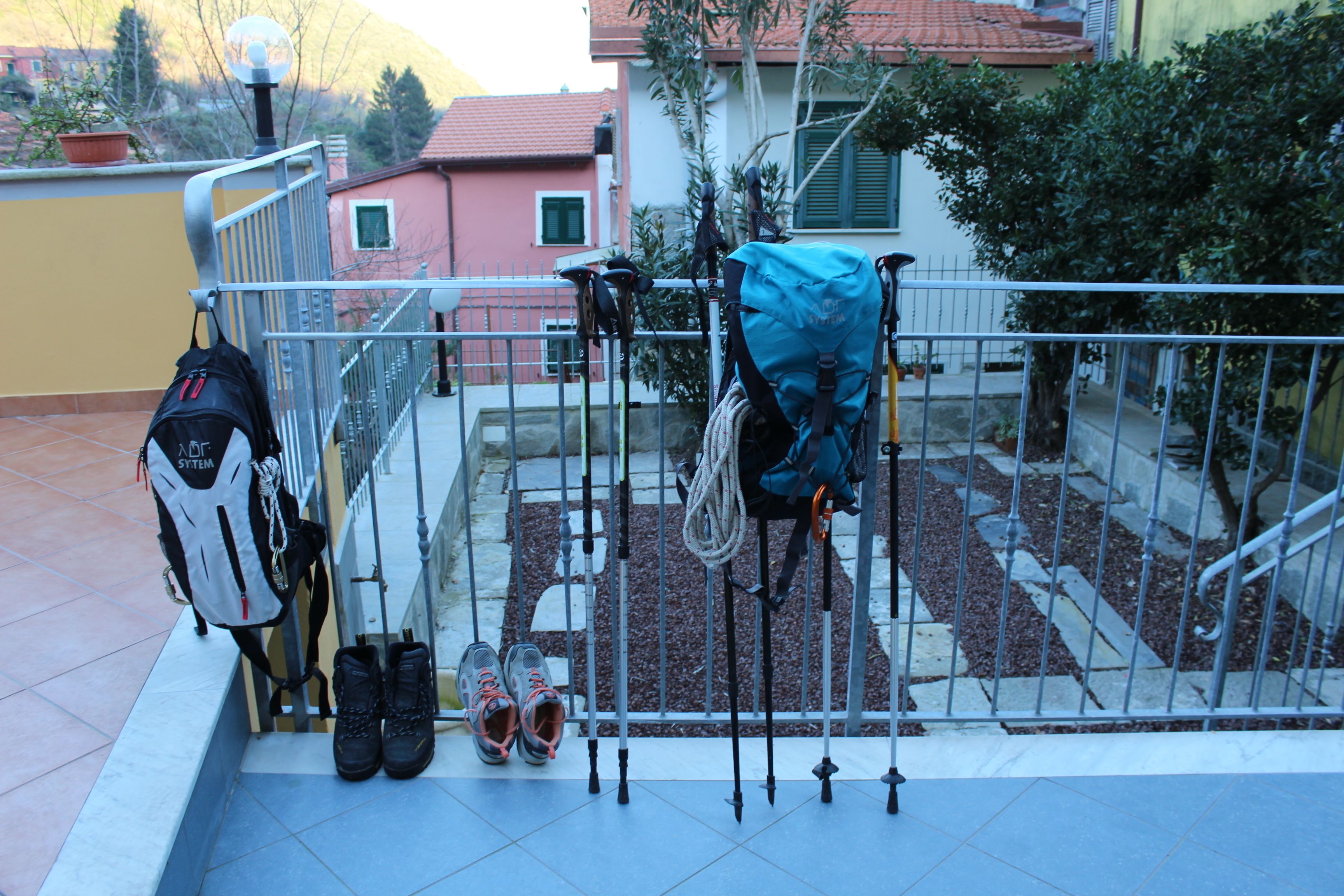 Un balcon avec une rambarde en métal, une paire de chaussures, un sac à dos et une corde d’escalade.