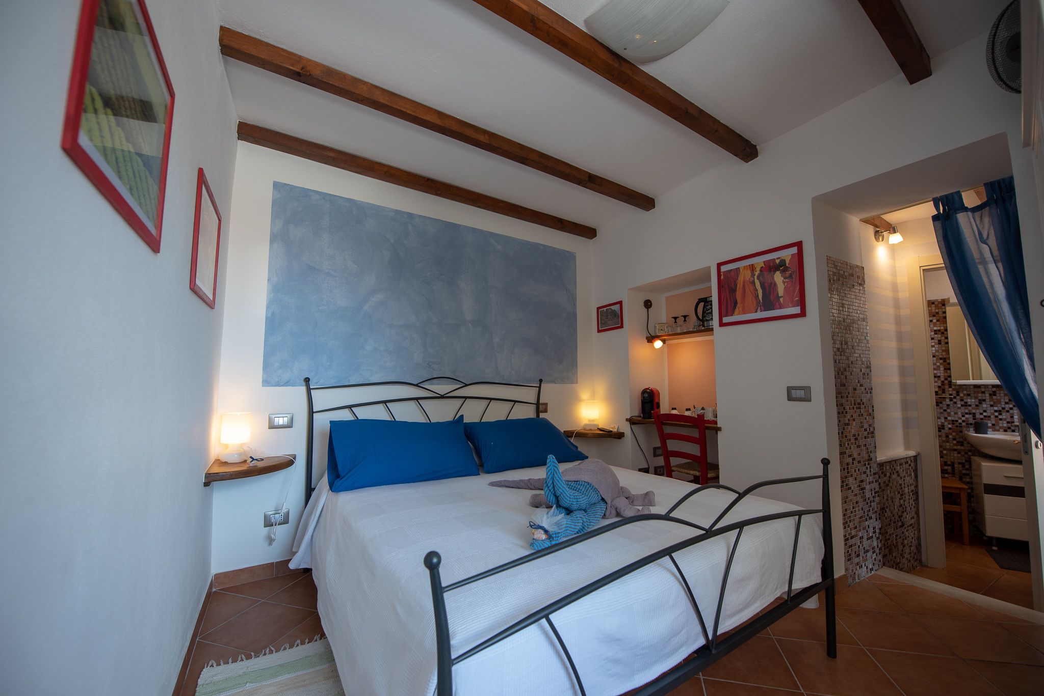 Un dormitorio con cama, mesitas de noche, una repisa en la pared y un baño visible a través de una puerta abierta.