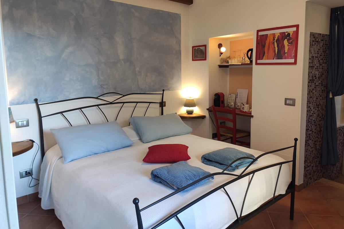 A bedroom with a bed, bedside table, lamp, and a small desk with a chair.