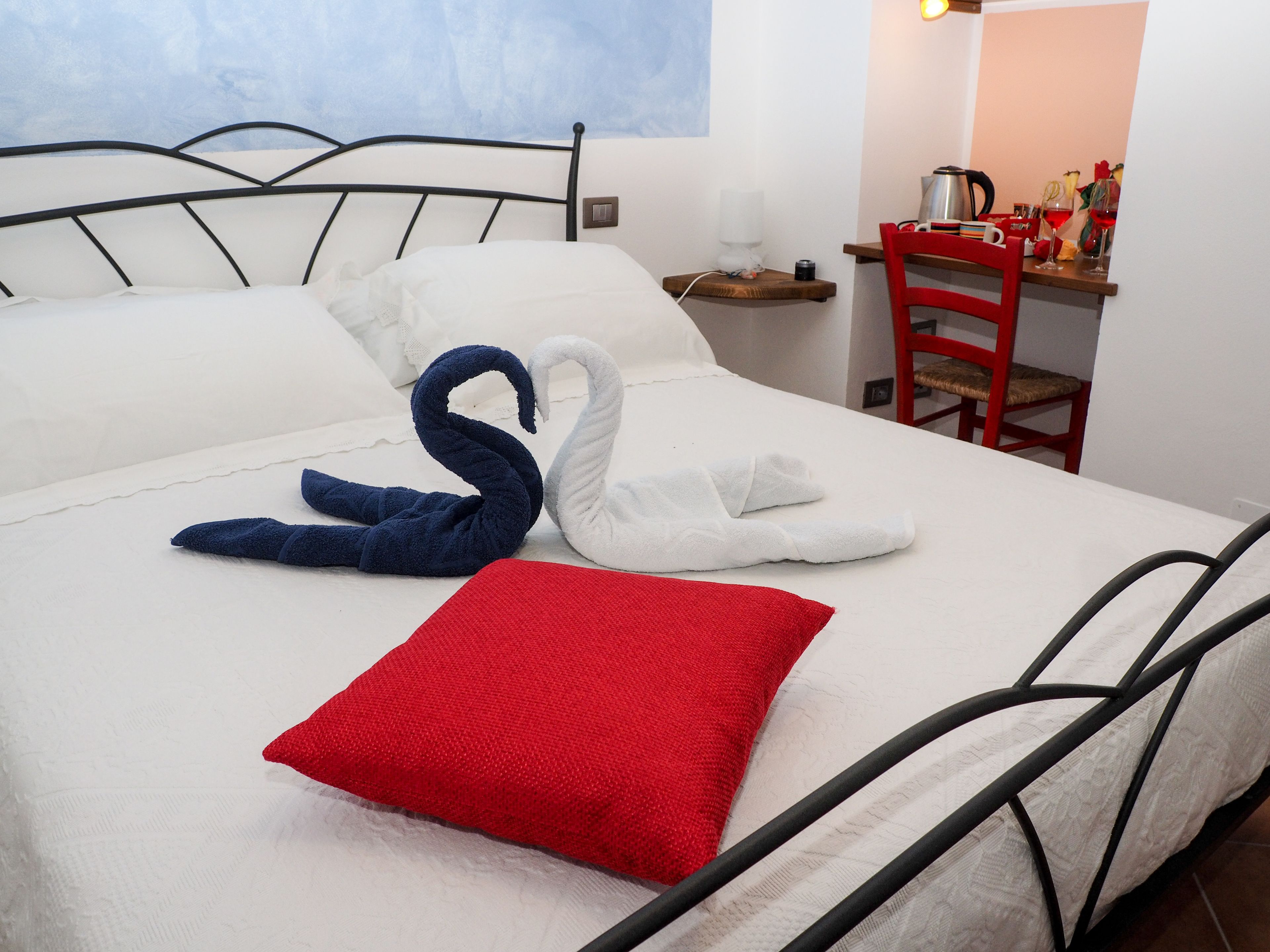 Una cama bien hecha con una almohada roja y dos toallas con forma de cisne.