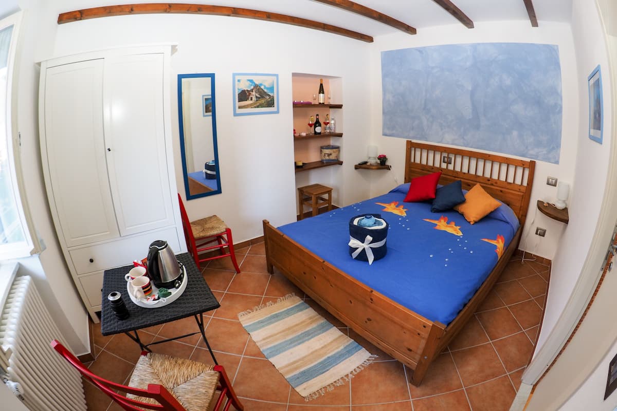 A bedroom with a wooden bed, a small table with a kettle, a chair, and a radiator.