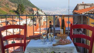 Un balcone con un tavolo apparecchiato per due, con vista su un paesaggio urbano caratterizzato da edifici con tetti rossi e una collina all'orizzonte.