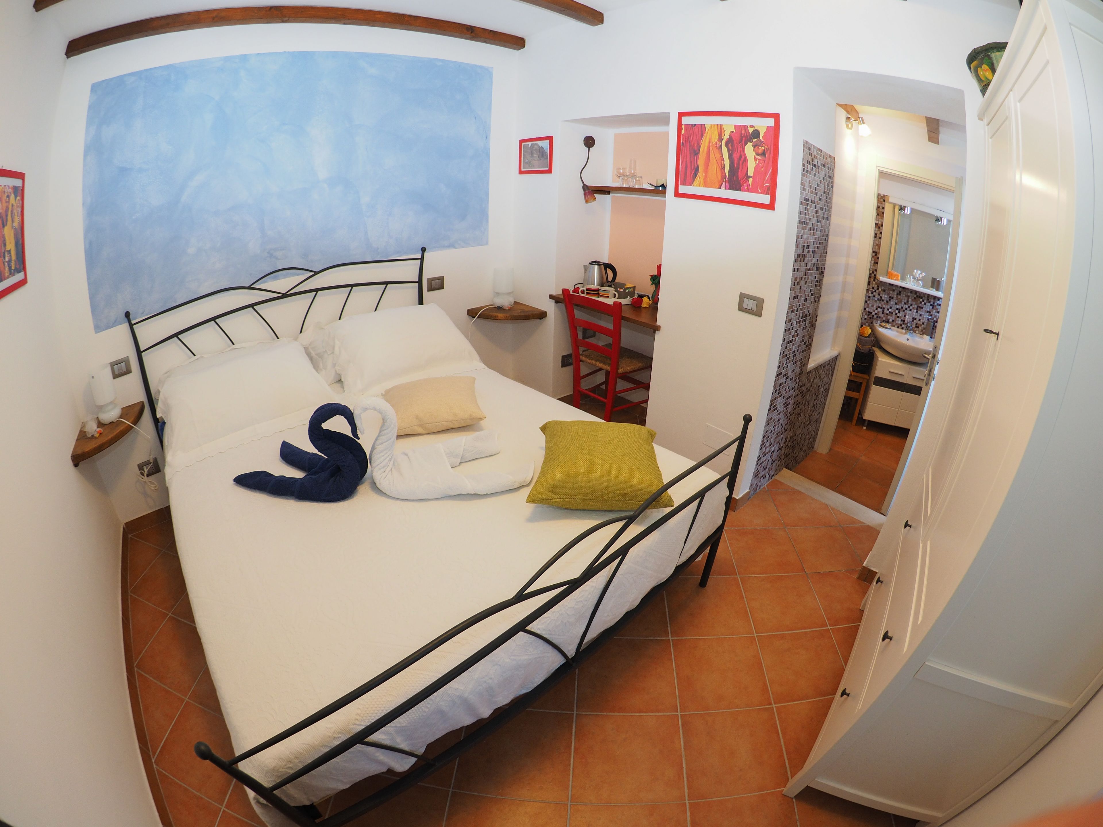 A bedroom with a bed, a red chair, a small table, and a bathroom visible through an open door.