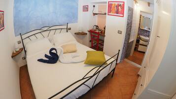 A bedroom with a bed, a red chair, a small table, and a bathroom visible through an open door.