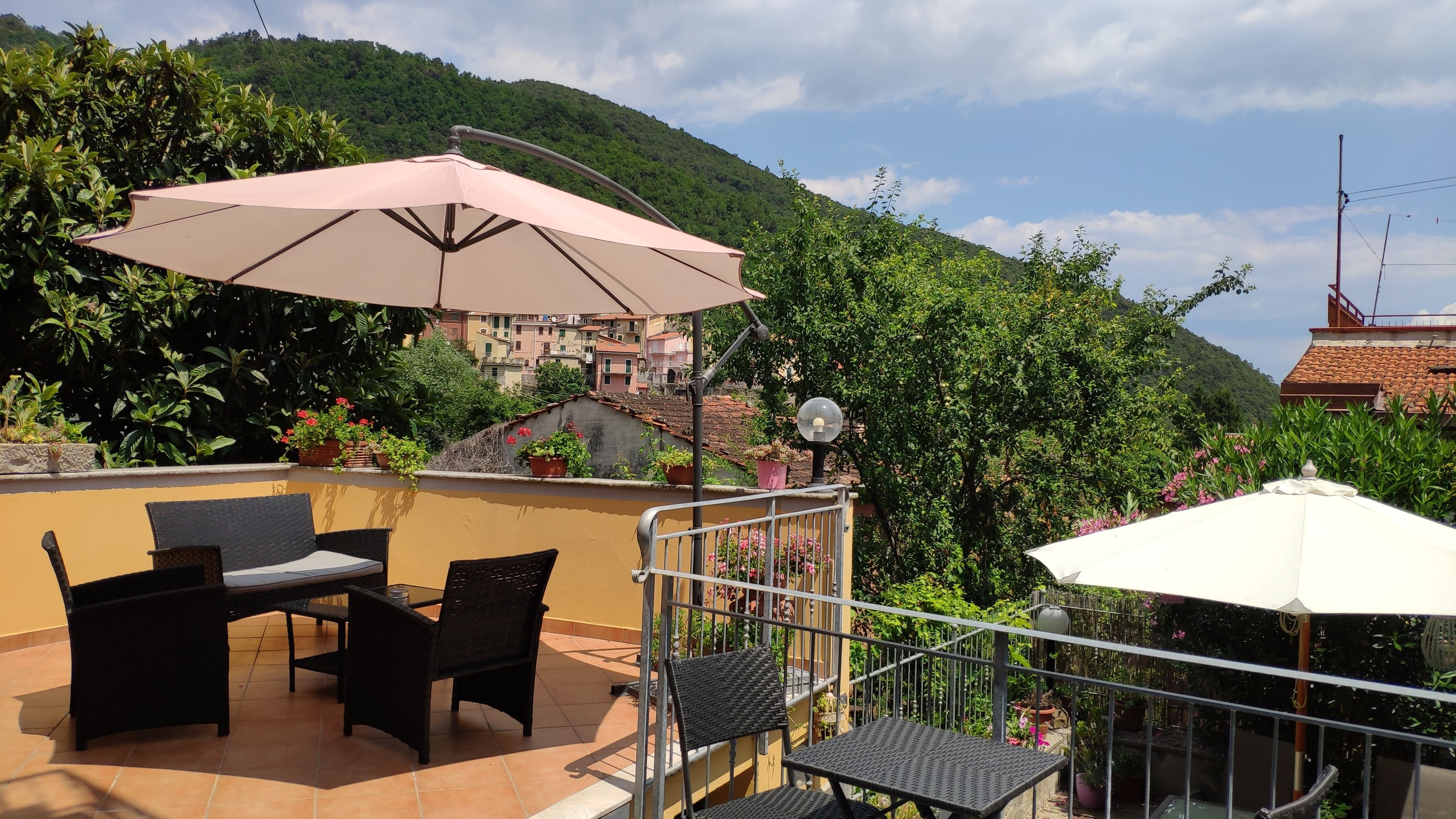 Una terraza con mobiliario exterior, un paraguas grande y plantas en macetas.