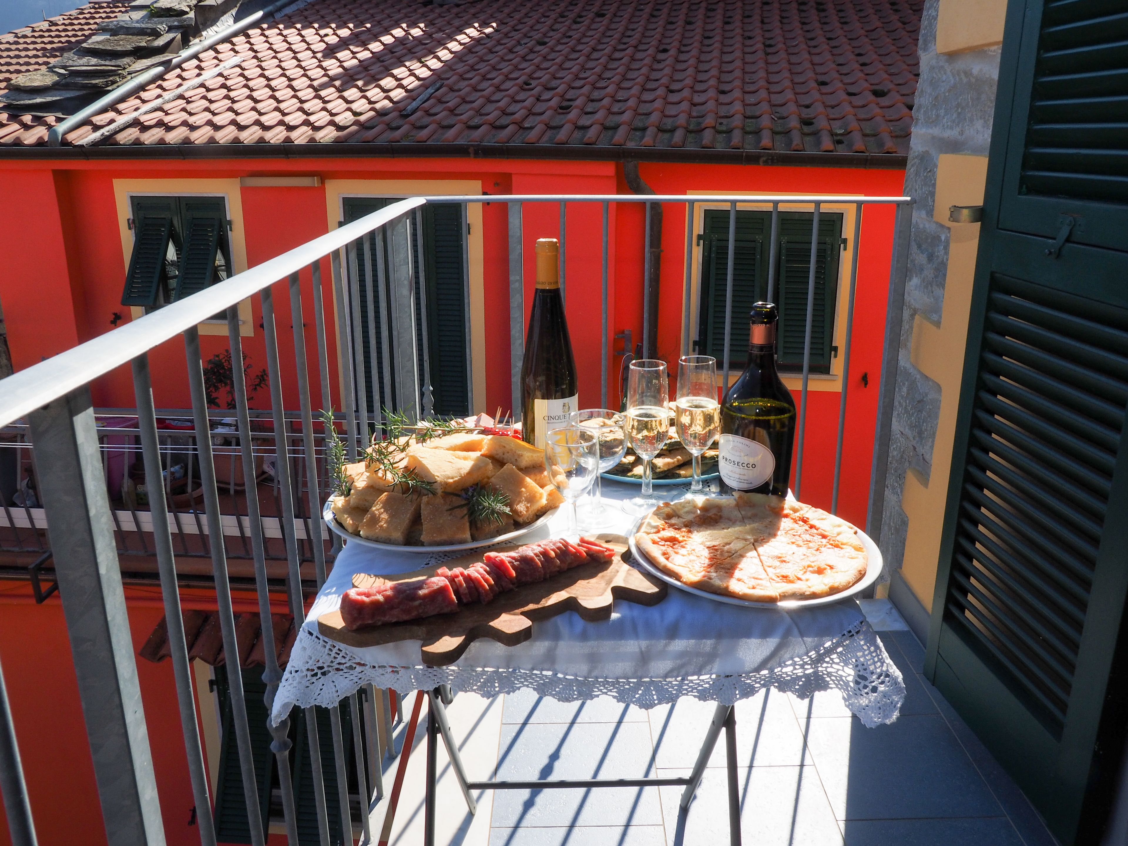 Un balcon avec une table dressée pour un repas, comprenant une pizza, une bouteille de vin et une assiette de charcuterie.