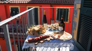 Un balcon avec une table dressée pour un repas, comprenant une pizza, une bouteille de vin et une assiette de charcuterie.