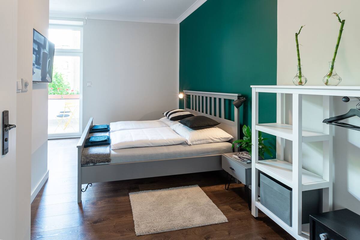 A bedroom with a bed, bedside table, nightstand, and a white shelving unit.