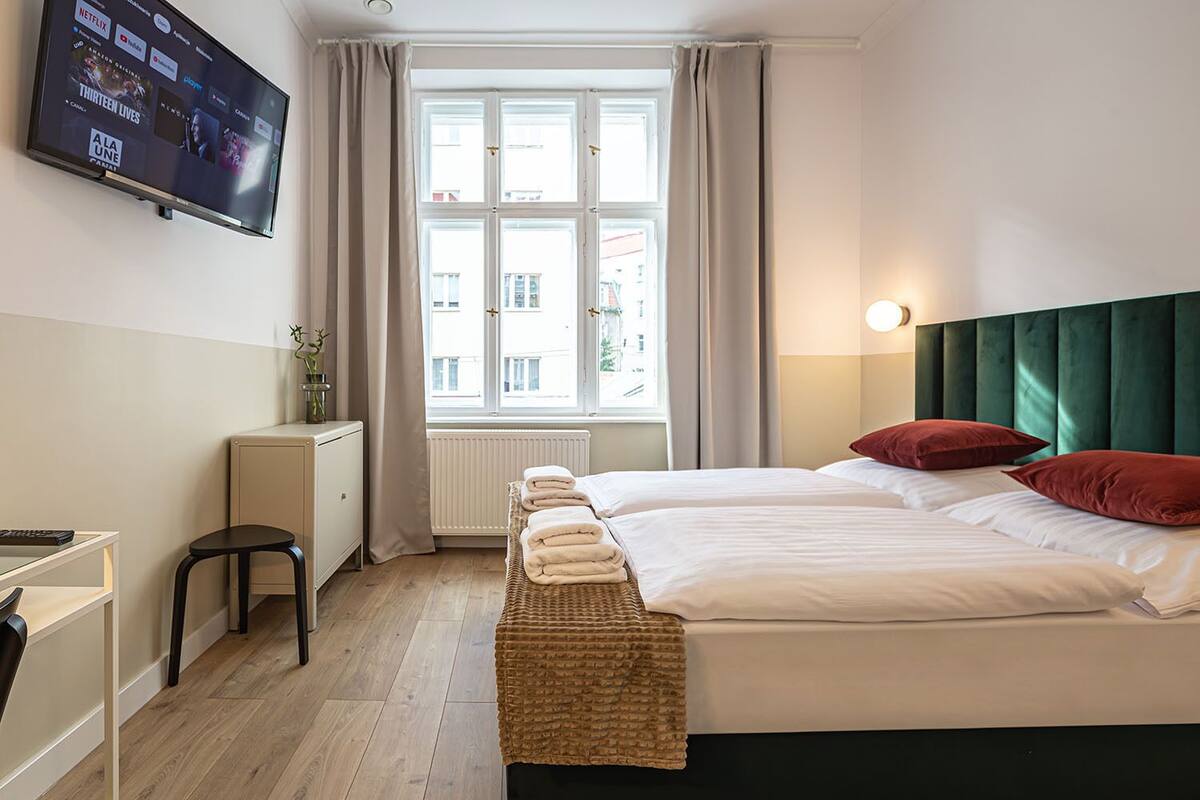 A hotel room with a bed, a desk, a television, and a window with curtains.