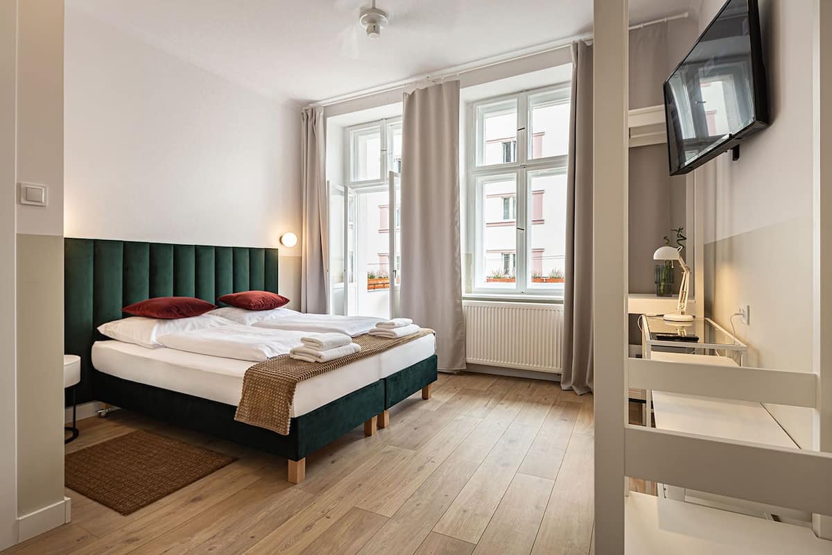 A modern hotel room with a large bed, a TV mounted on the wall, and a view of the city through large windows.