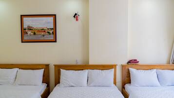 A hotel room with three beds, a framed picture of a cityscape, and a small red object on the wall.