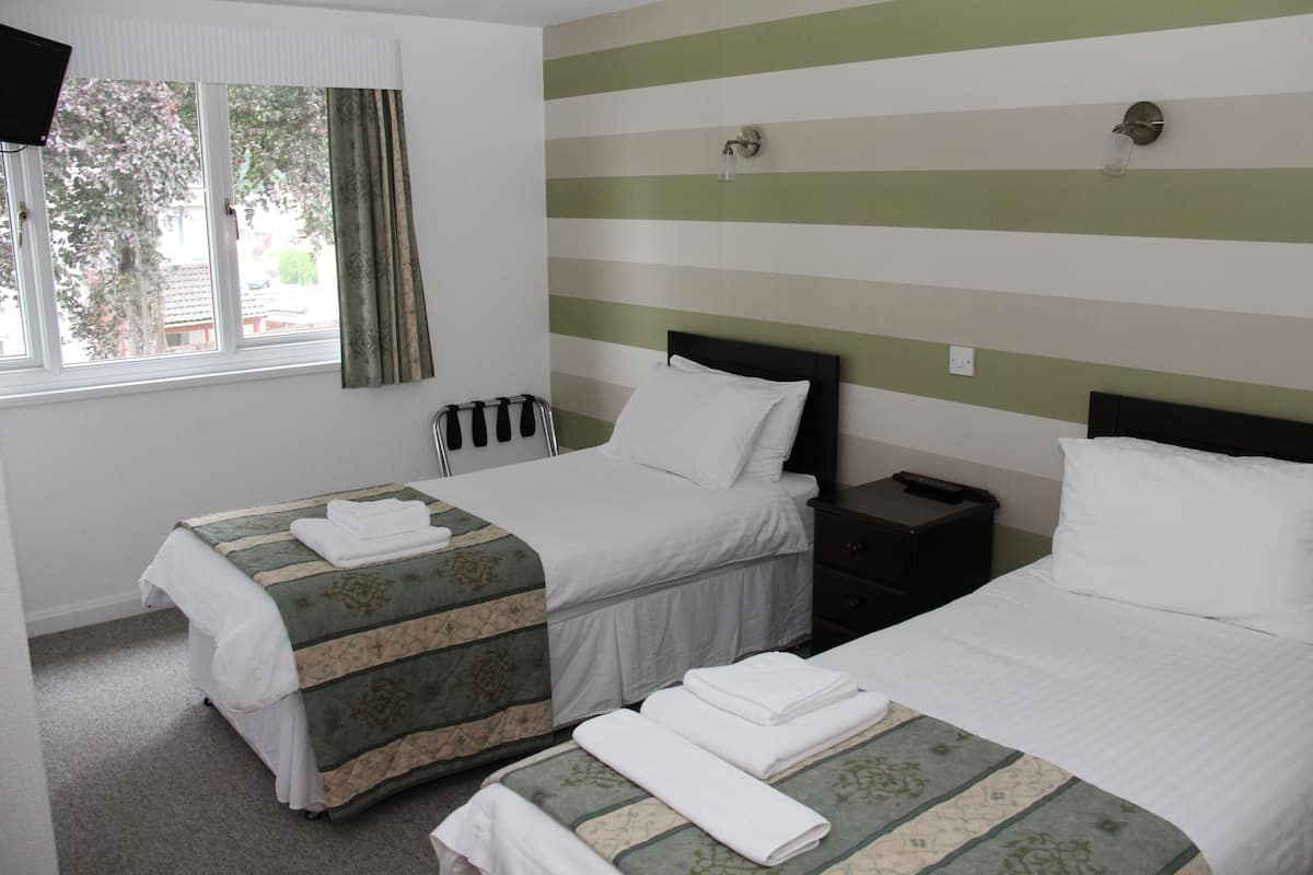 A hotel room with two beds, a window with curtains, a bedside table, and a wall-mounted light fixture.