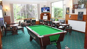 A pool table in a room with multiple chairs, a television, and a view of trees through large windows. - Ravenswood Country Club Legion Scotland (Banchory)