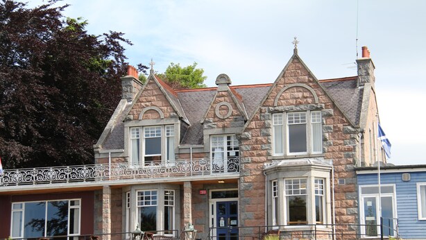 A stone building with a balcony, large windows, and a flag. - Ravenswood Country Club Legion Scotland (Banchory)