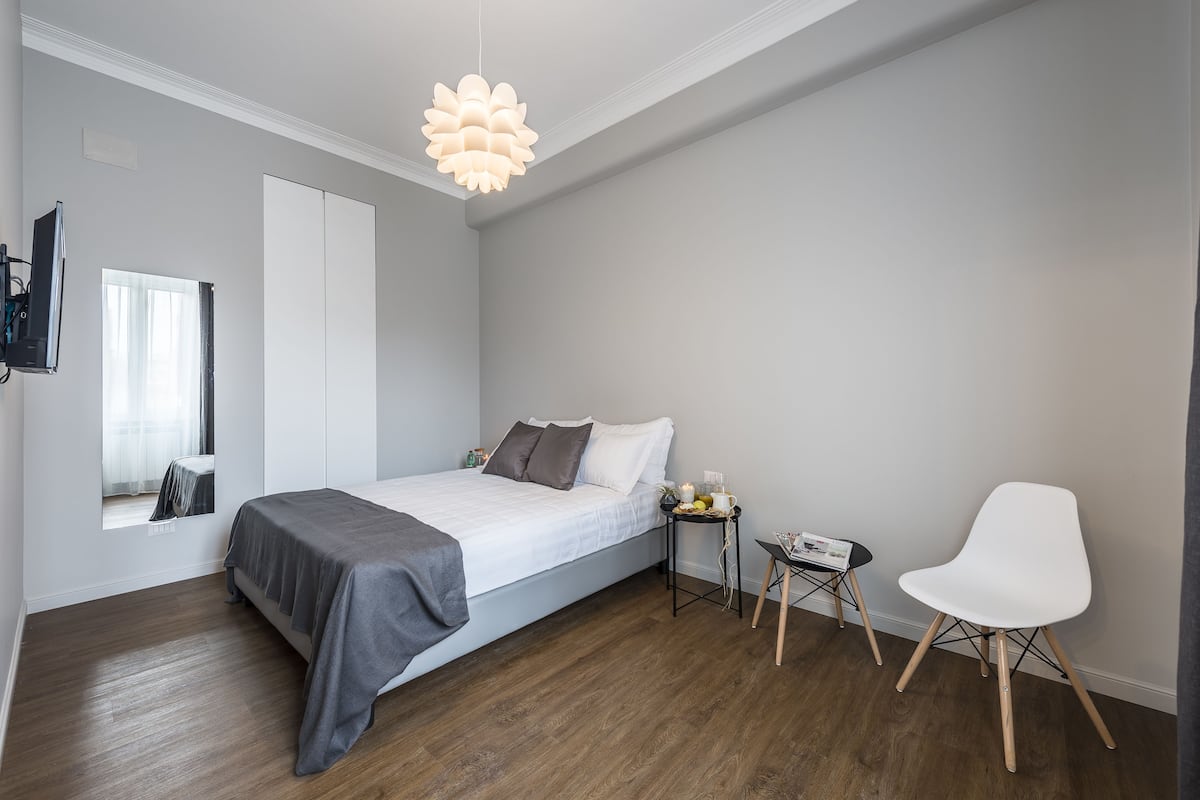 A modern bedroom with a bed, bedside table, chair, and a unique ceiling light fixture.