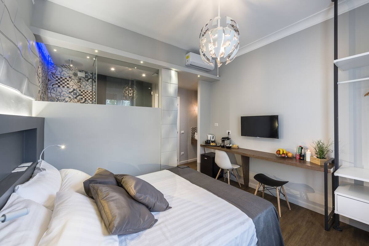 A modern bedroom with a bed, desk, chair, and a TV.