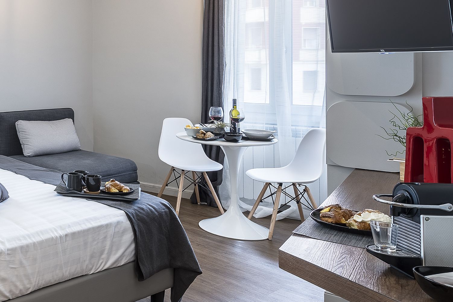 Hotellihuone, jossa on sänky, pieni ruokapöytä tuoleineen, televisio ja pieni keittotila.