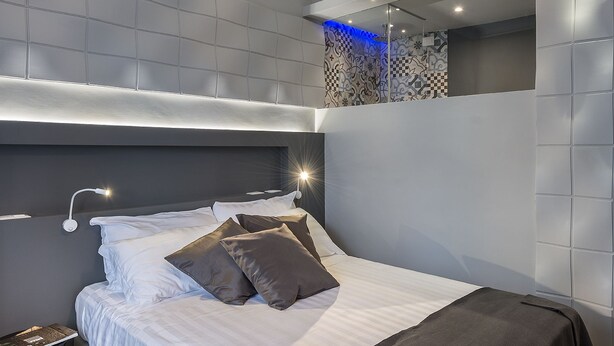 A modern bedroom with a large bed, a bedside table, and a wall-mounted light fixture. - Z-ArchSuiTes (Rome)