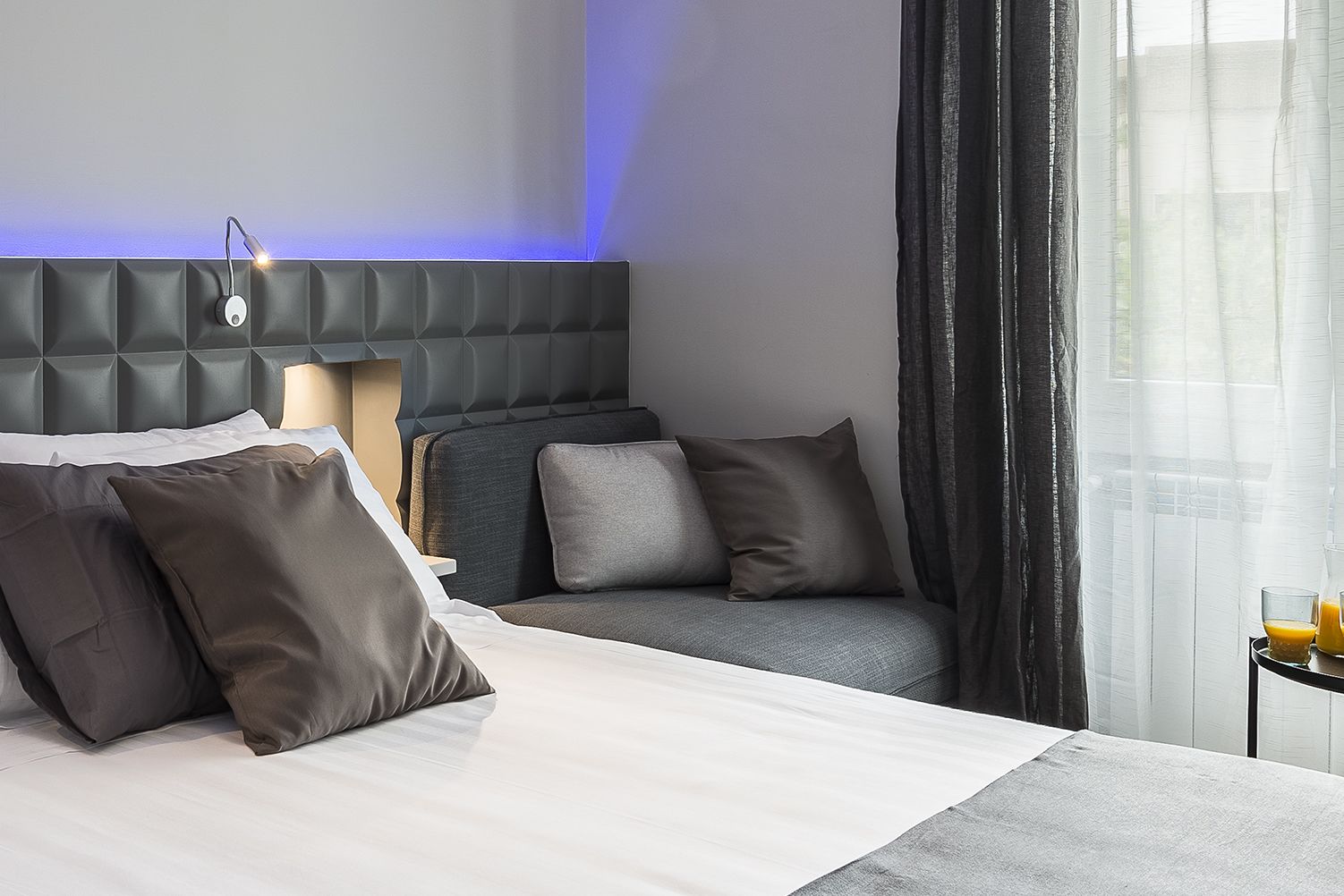 A hotel room with a bed, a sofa, and a table with a glass of orange juice.