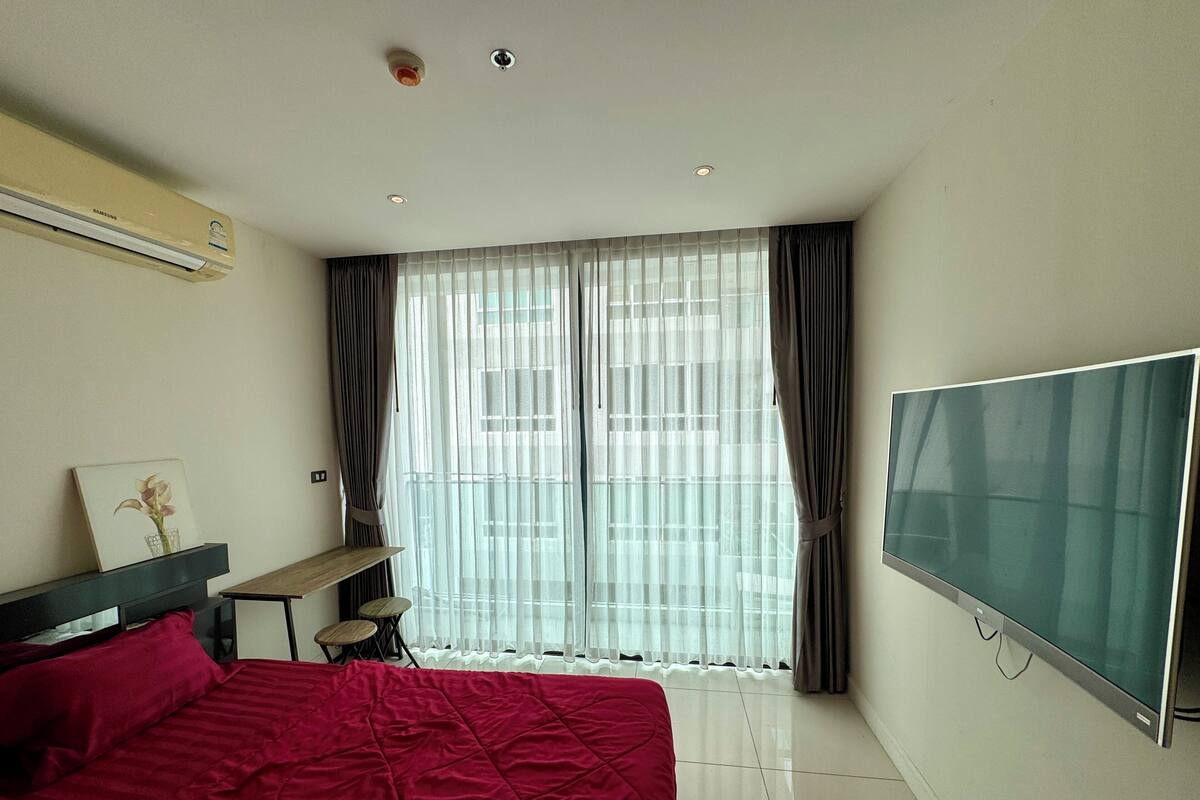 A bedroom with a bed, a TV, a desk, and a window with curtains.