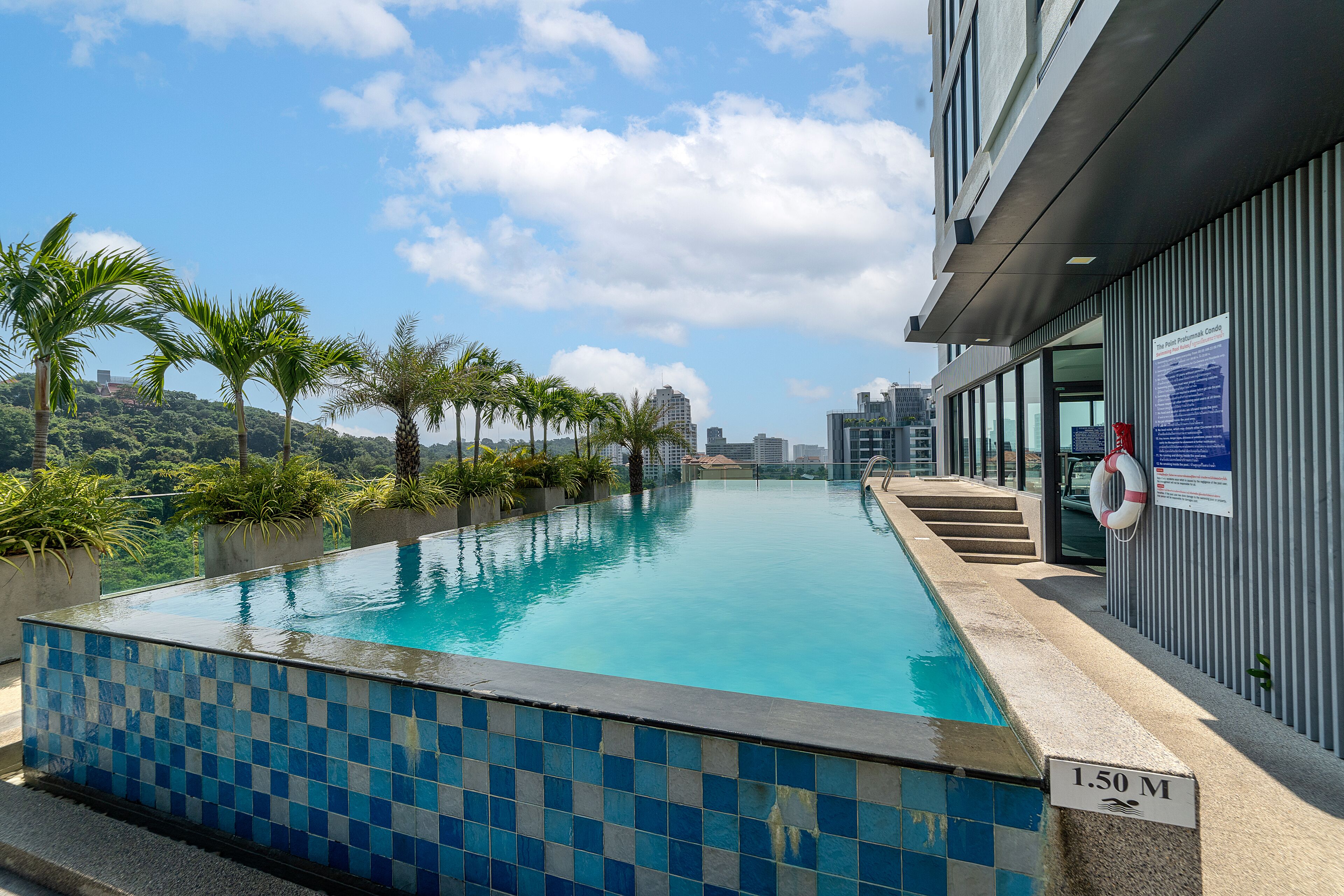 Una piscina sense fi amb rajoles blaves, palmeres i vista als edificis de la ciutat.