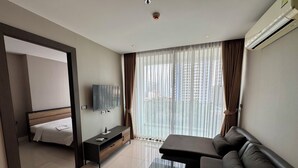 A modern hotel room with a bed, a TV, a sofa, a coffee table, and a large window with curtains. - The Point Pratumnak by PSR ASIA (Pattaya)