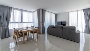 A modern living room with a dining area, grey curtains, a grey sofa, and a flat-screen TV. - The Point Pratumnak by PSR ASIA (Pattaya)