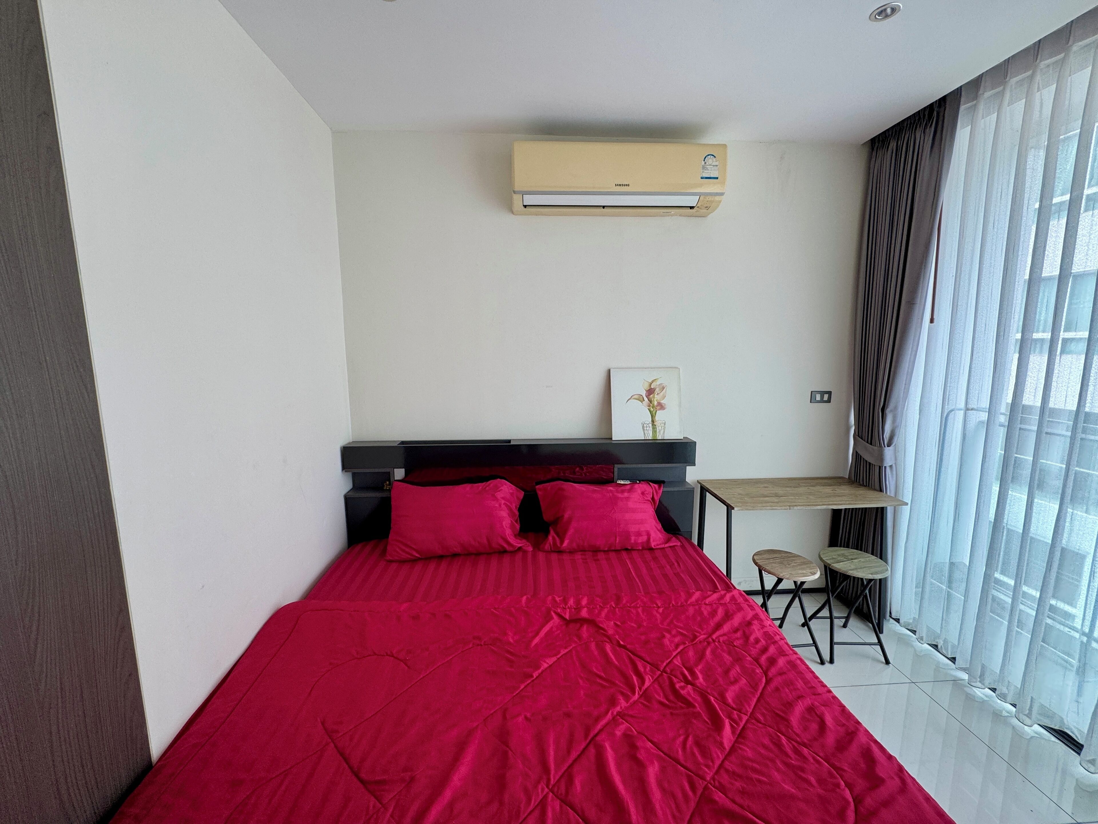 A bedroom with a bed, a small table, and an air conditioning unit.