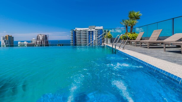 A rooftop infinity pool with clear blue water, lounge chairs, and a view of tall buildings. - The Point Pratumnak by PSR ASIA (Pattaya)