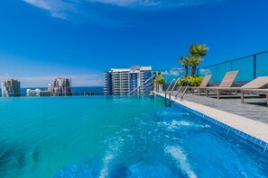 A rooftop infinity pool with clear blue water, lounge chairs, and a view of tall buildings. - The Point Pratumnak by PSR ASIA (Pattaya)