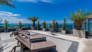 A rooftop terrace with lounge chairs, potted plants, and a view of the ocean and city skyline. - The Point Pratumnak by PSR ASIA (Pattaya)