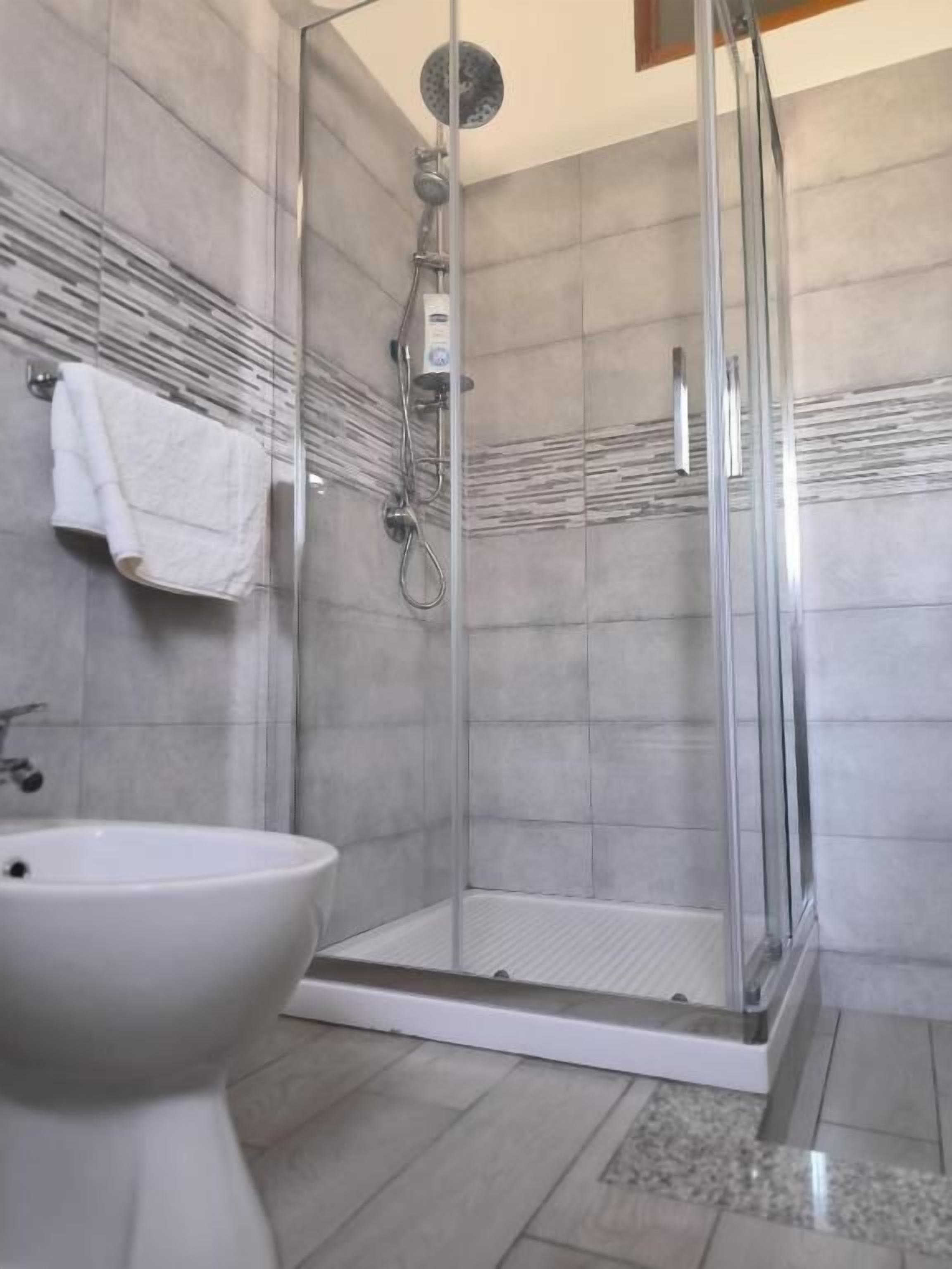 A shower with a glass door, a white sink, and a towel hanging on the wall.