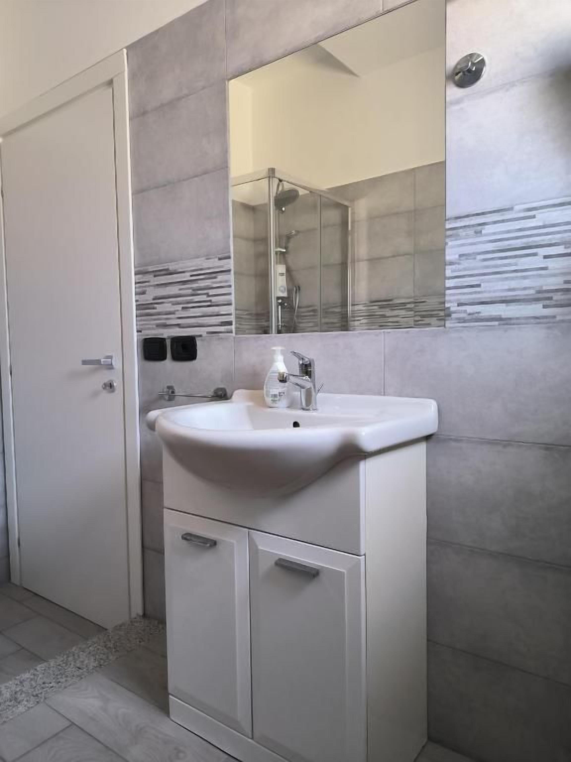 Un bagno con un lavandino bianco, uno specchio e una doccia.
