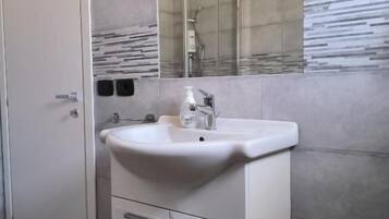 Un bagno con un lavandino bianco, uno specchio e una doccia.