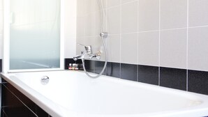 A bathroom with a white bathtub, a showerhead, and black and white tiled walls. - Art Apartment Bandinelli (Florence)
