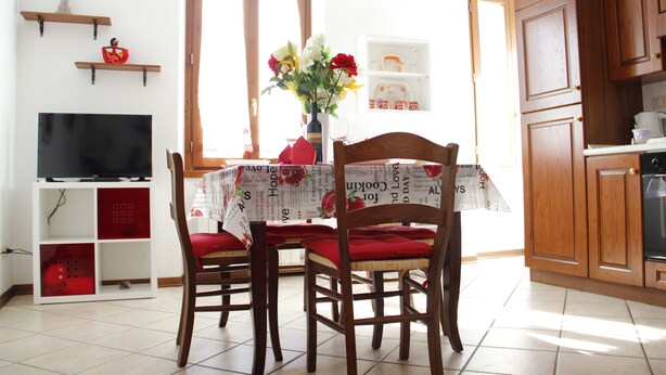 A dining area with a table set for two, a television on a stand, and wooden cabinets in the background. - Art Apartment Bandinelli (Florence)