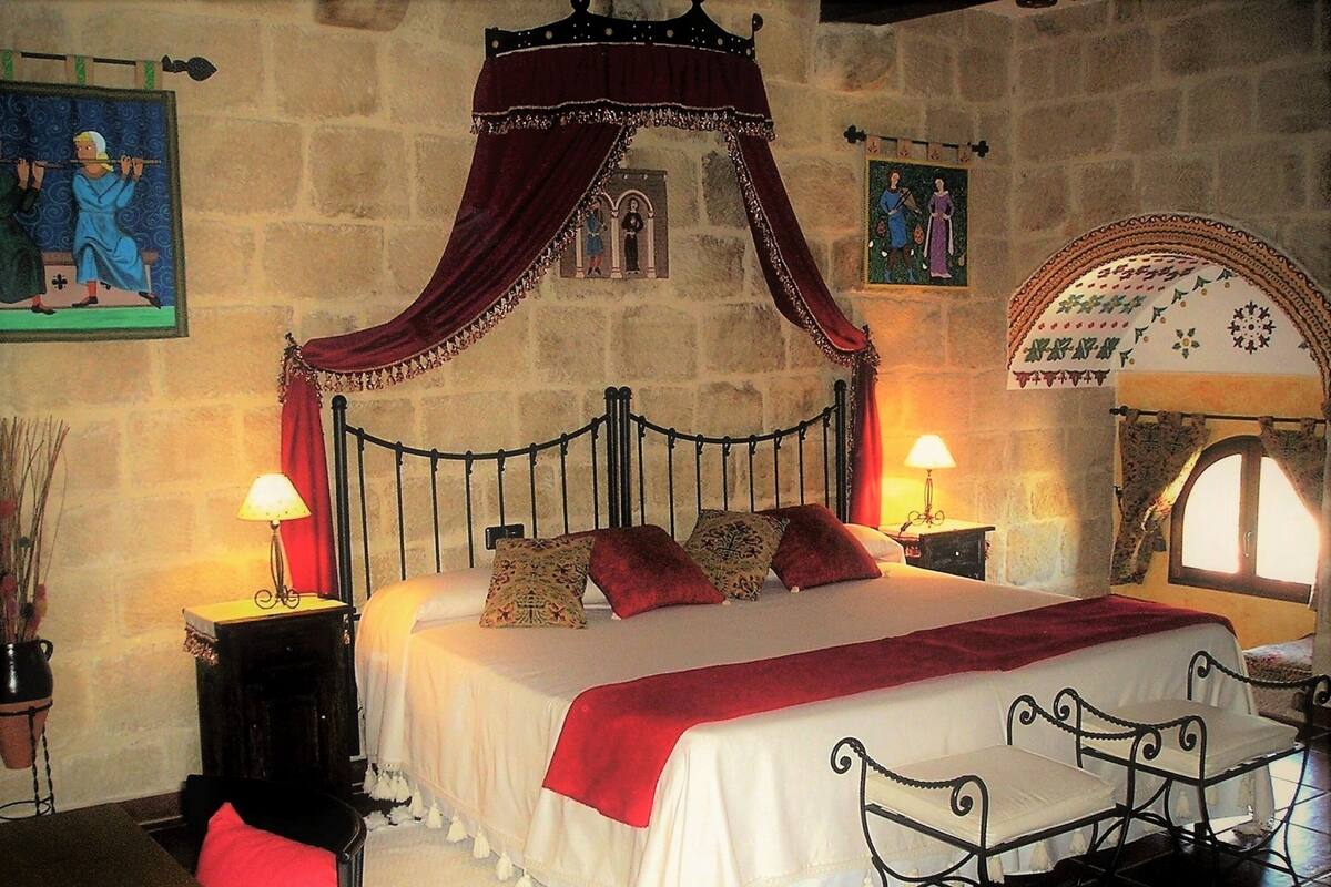 A bedroom with a four-poster bed, a stone wall, and a window with a decorative arch.