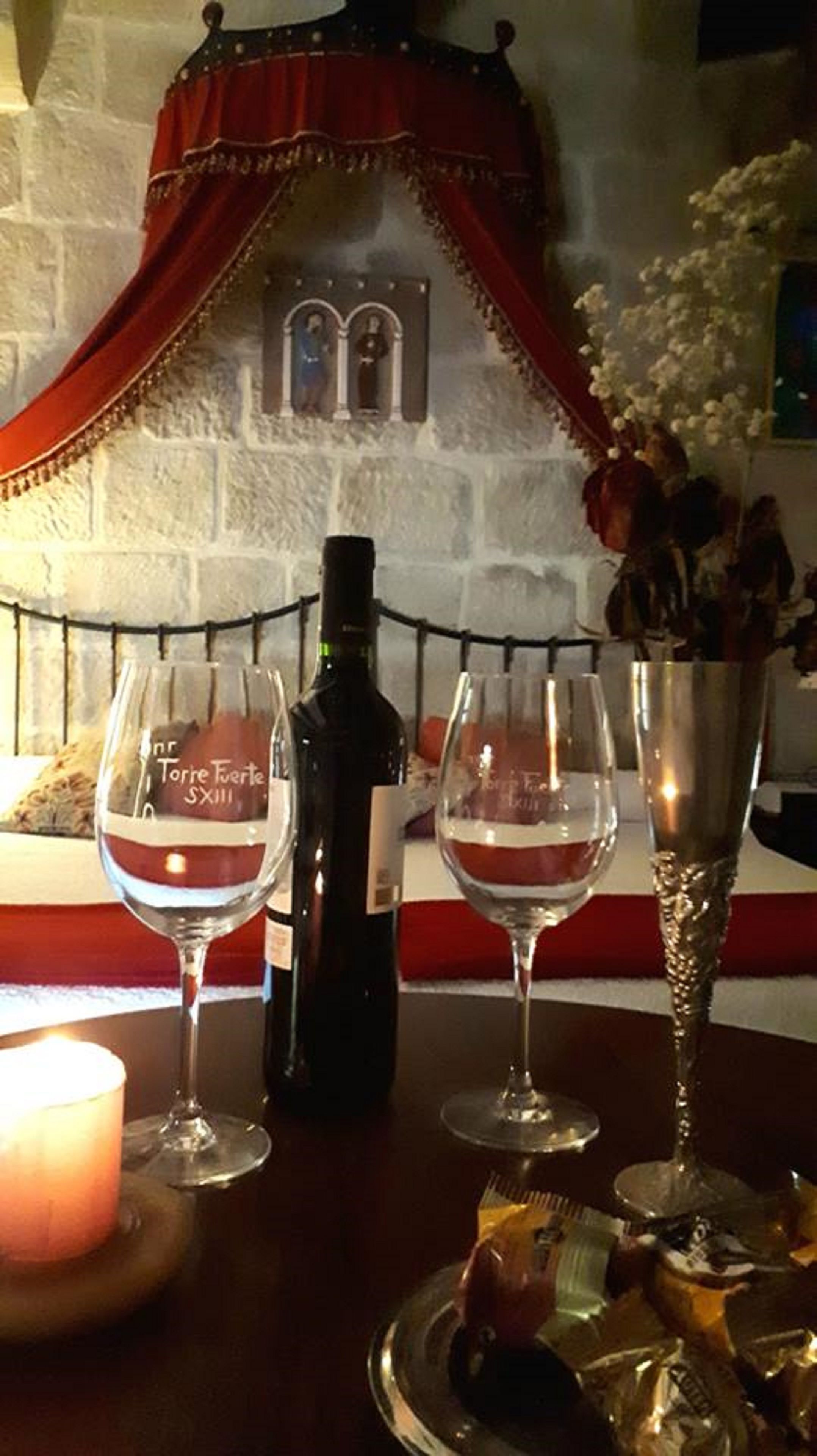 Uma mesa com duas taças de vinho, uma garrafa de vinho, uma vela e um vaso decorativo com flores.