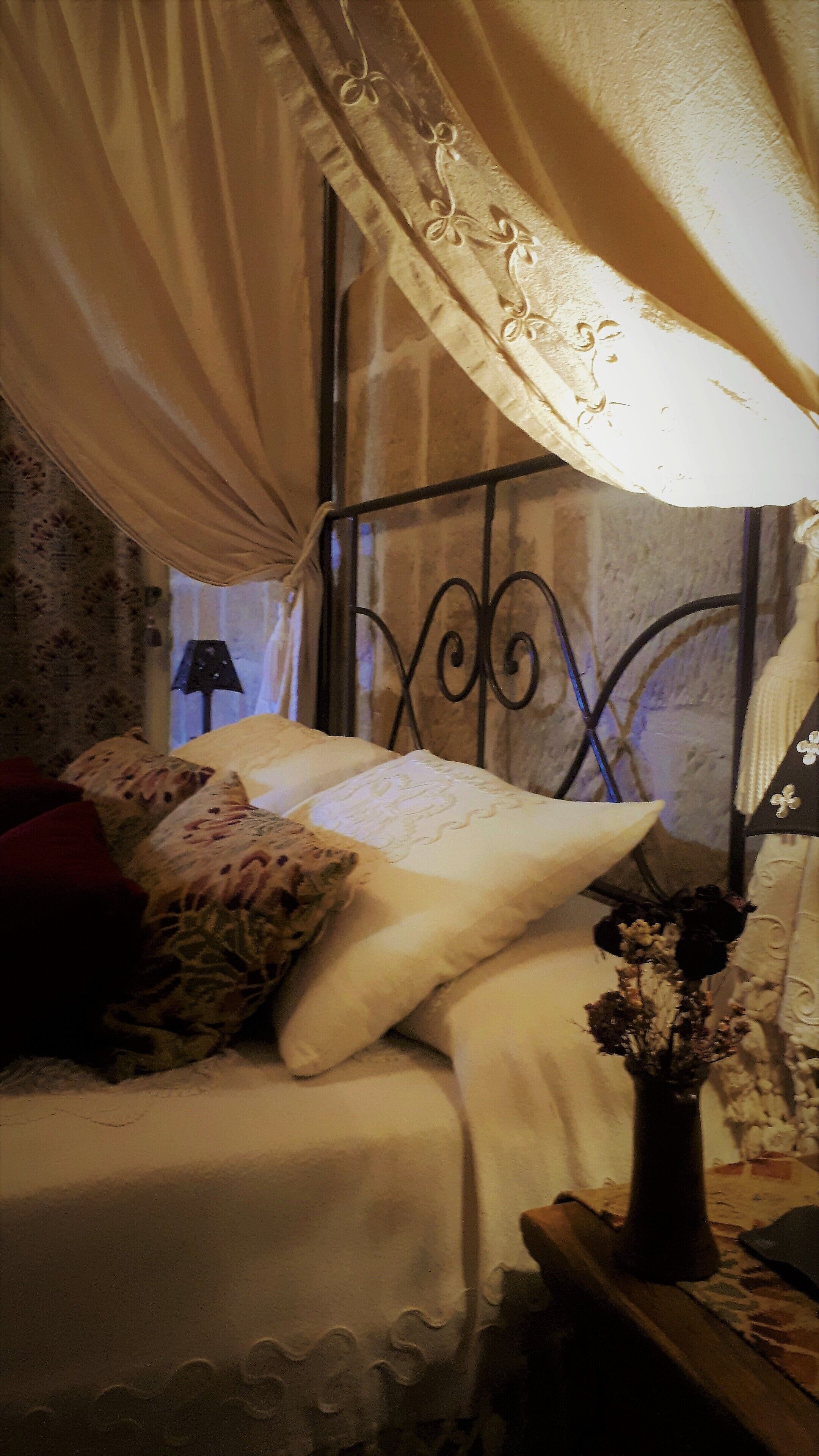 A bed with a canopy, a vase with flowers, and a lamp.