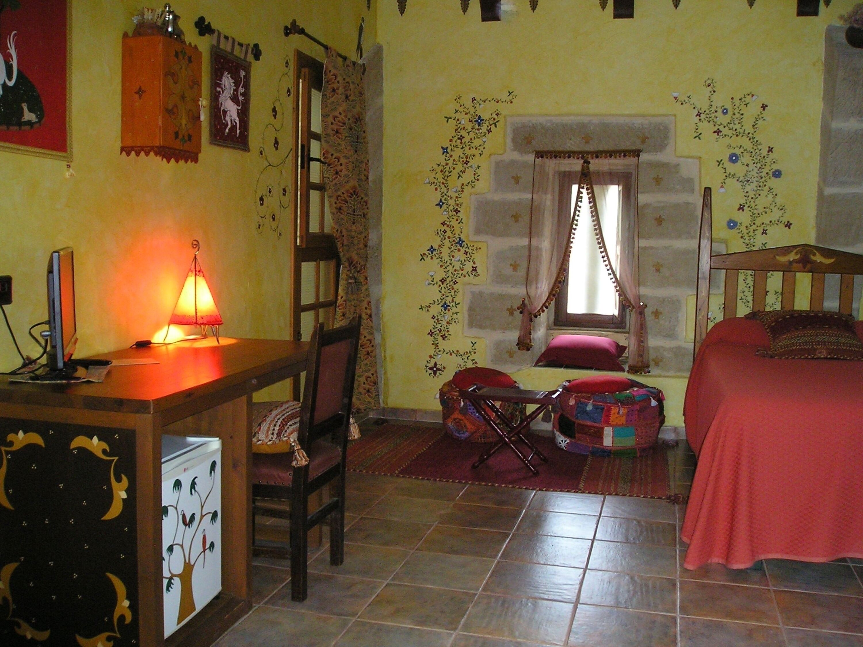 Una stanza con un letto, una scrivania con lampada, una sedia e una finestra con tende.