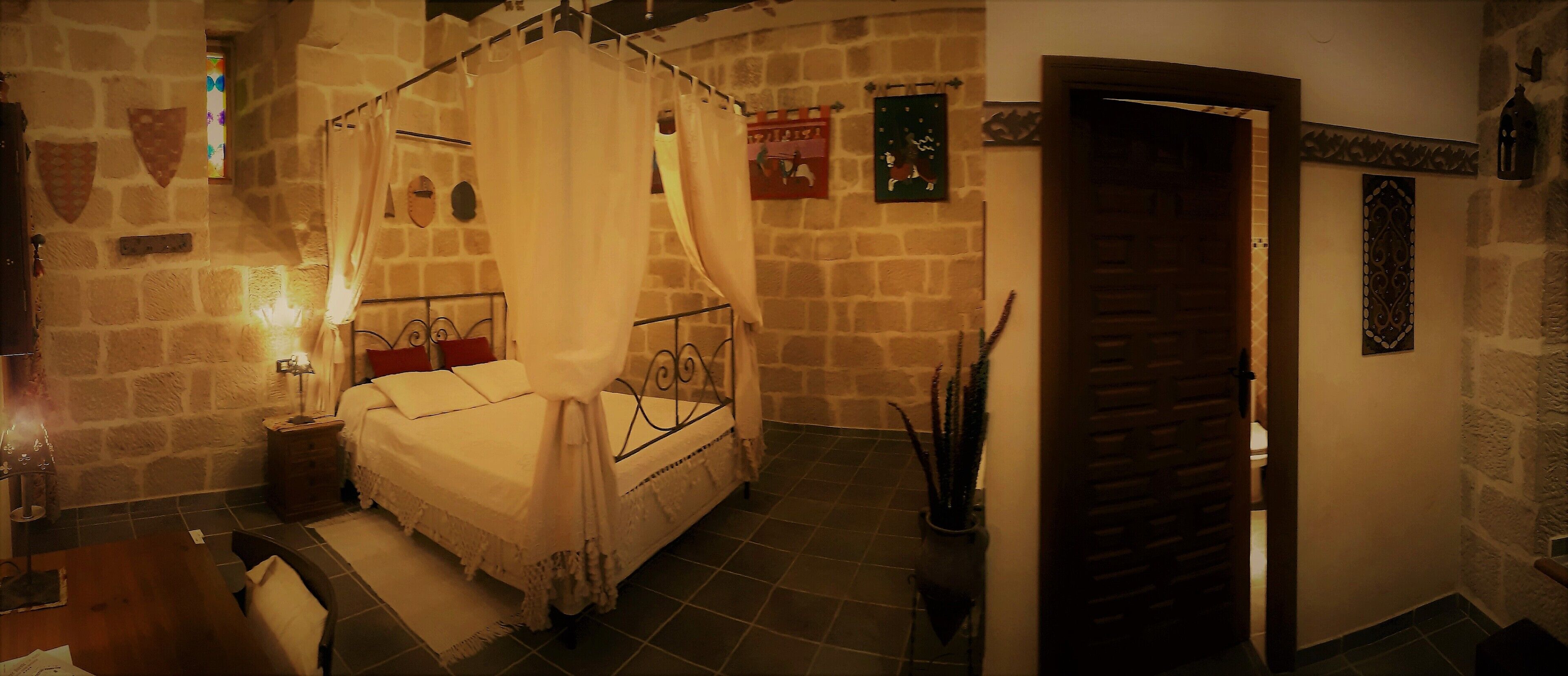A bedroom with a four-poster bed, stone walls, and a wooden door.
